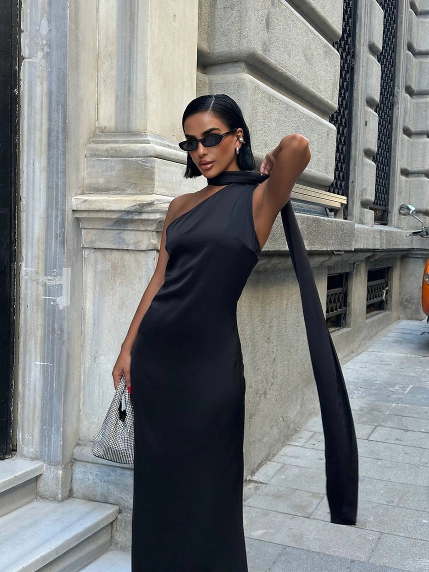 Woman in a black one-shoulder dress standing against a stone building. Standpoint Top