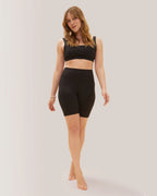 Woman in Rose Boreal black athletic wear and cap standing outdoors with white in the background