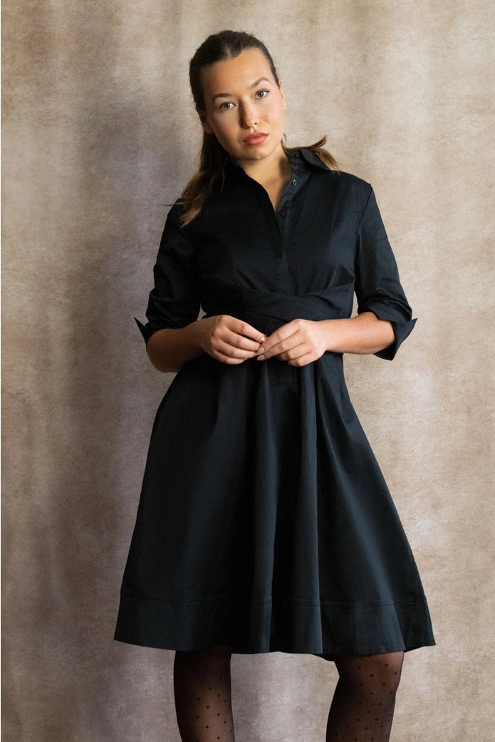 Woman wearing a black dress against a neutral background ANNICK